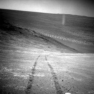 A black and white photograph of a rocky landscape with black tracks visible on the ground